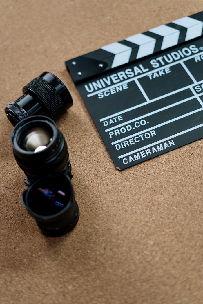 Flat lay of vintage film equipment including lenses and clapboard on cork surface.